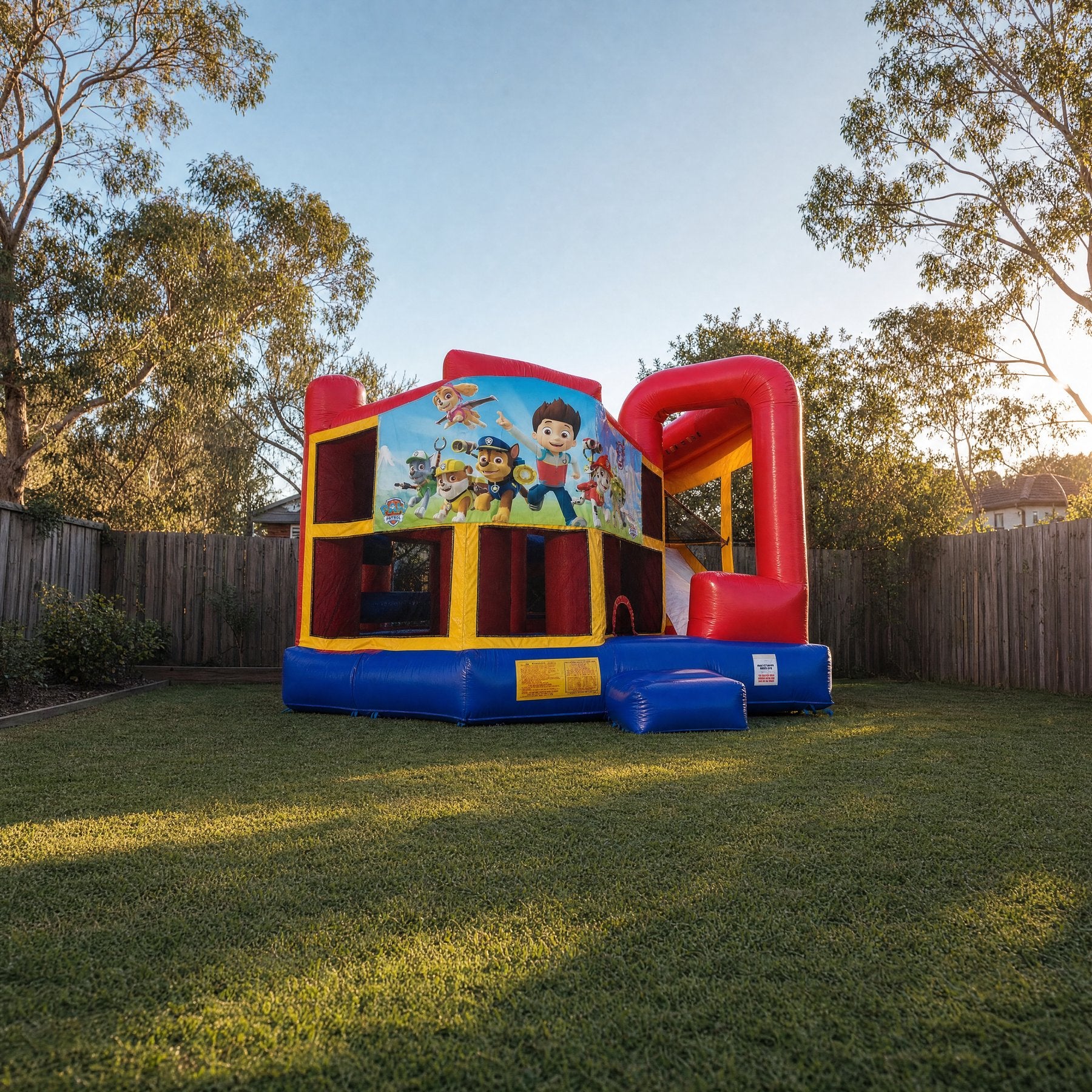 Wide backyard view of the 5in1 Banner Castle Combo showing its true size (shown with the Paw Patrol banner, choose your theme at booking)