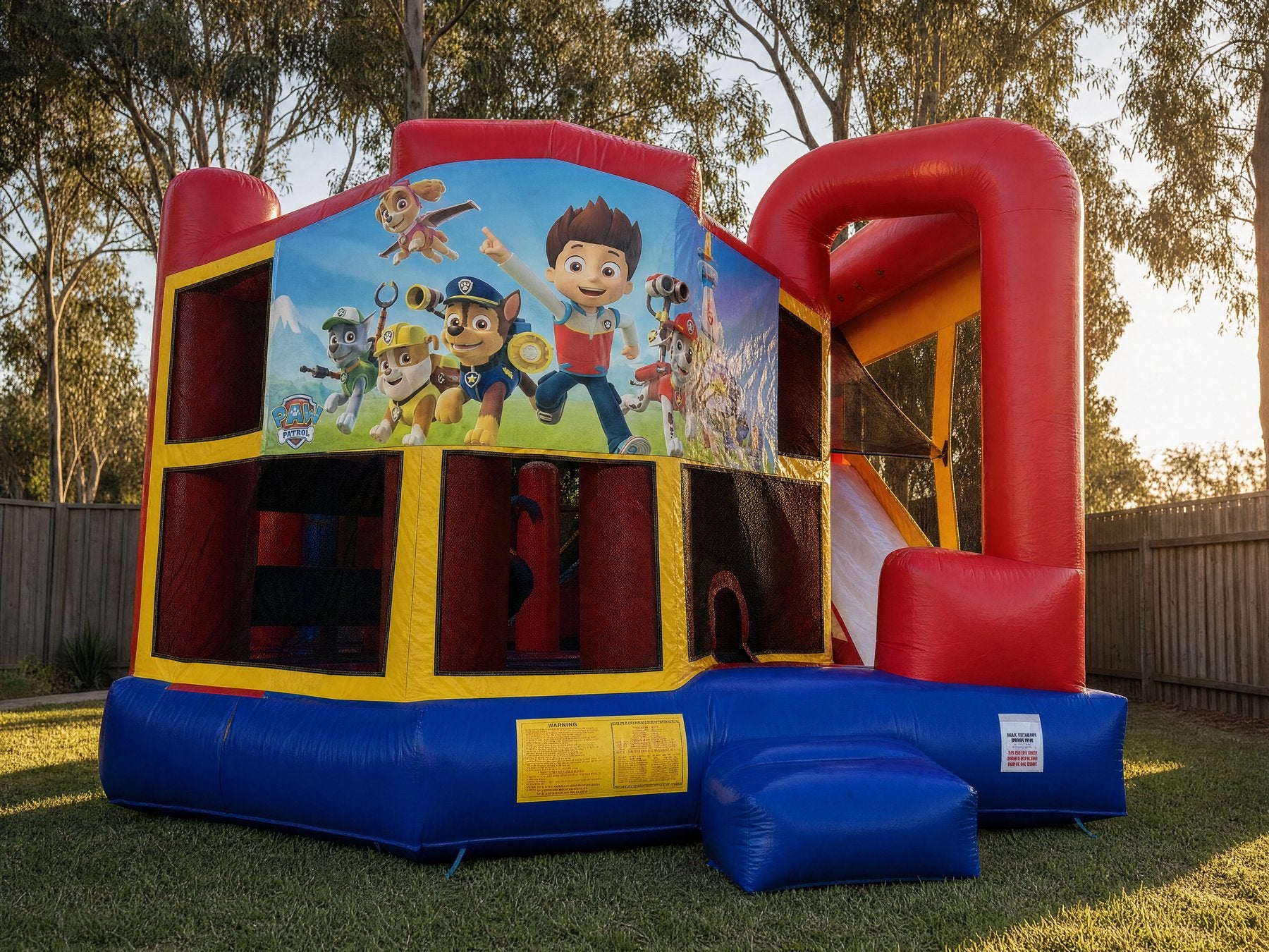 Landscape view of the 5in1 Banner Castle Combo in a backyard (shown with the Paw Patrol banner, choose your theme at booking)