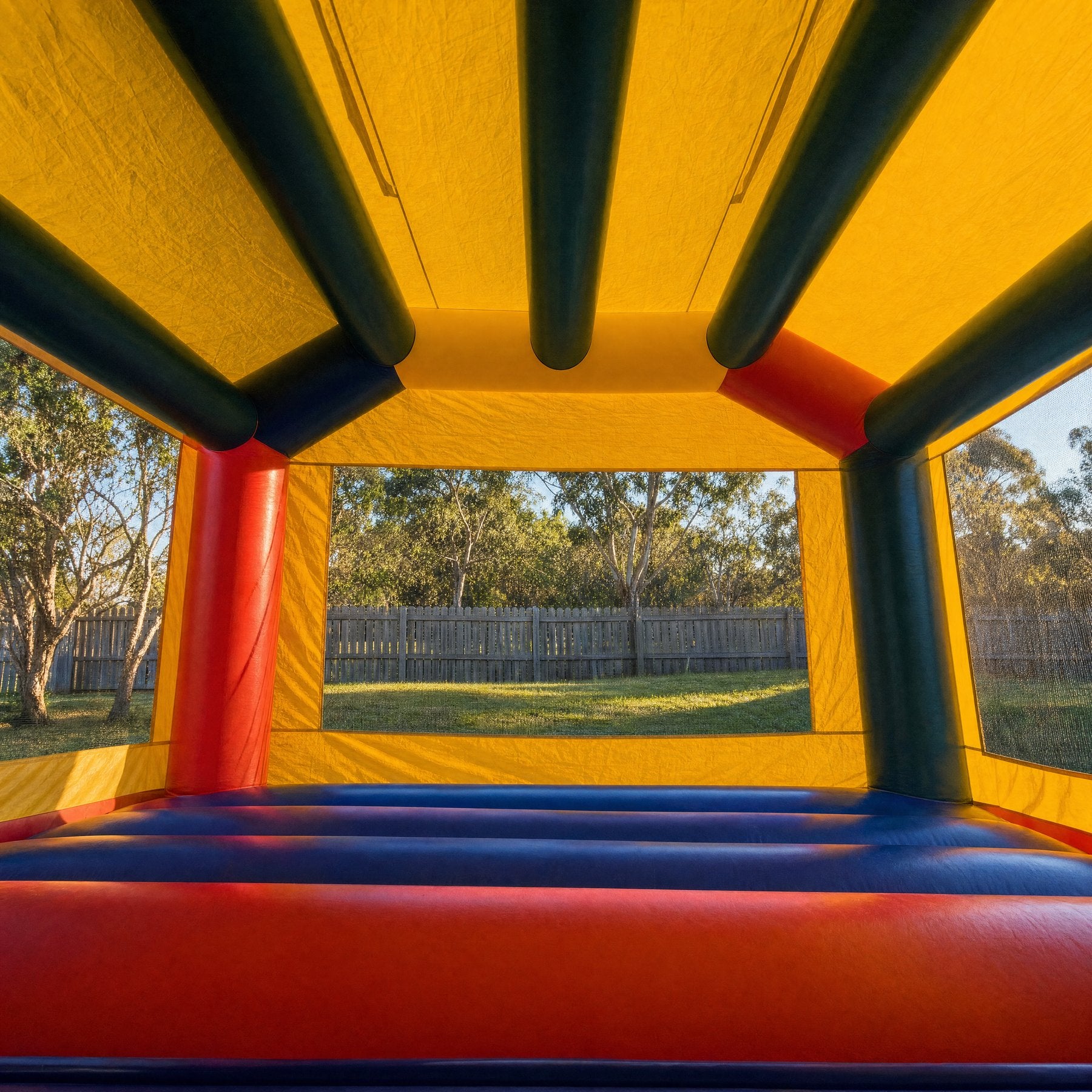 Interior view of an adult jumping castle looking out through a mesh window to a backyard