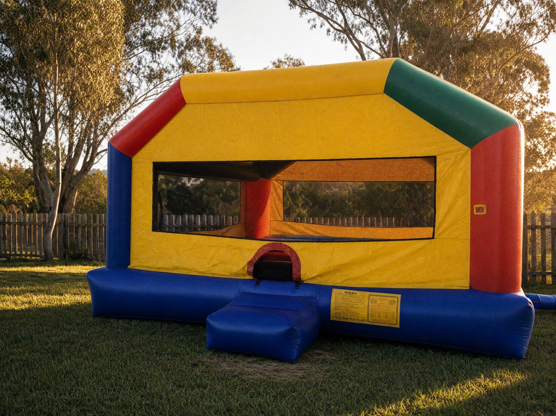 Wide view of a yellow and red adult jumping castle in a backyard at golden hour