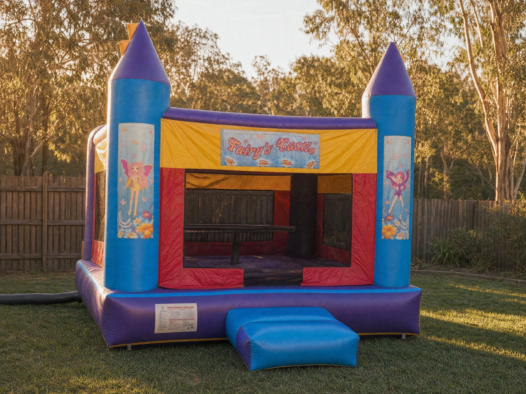 Wide view of a purple and blue AM Banner jumping castle in a backyard at golden hour