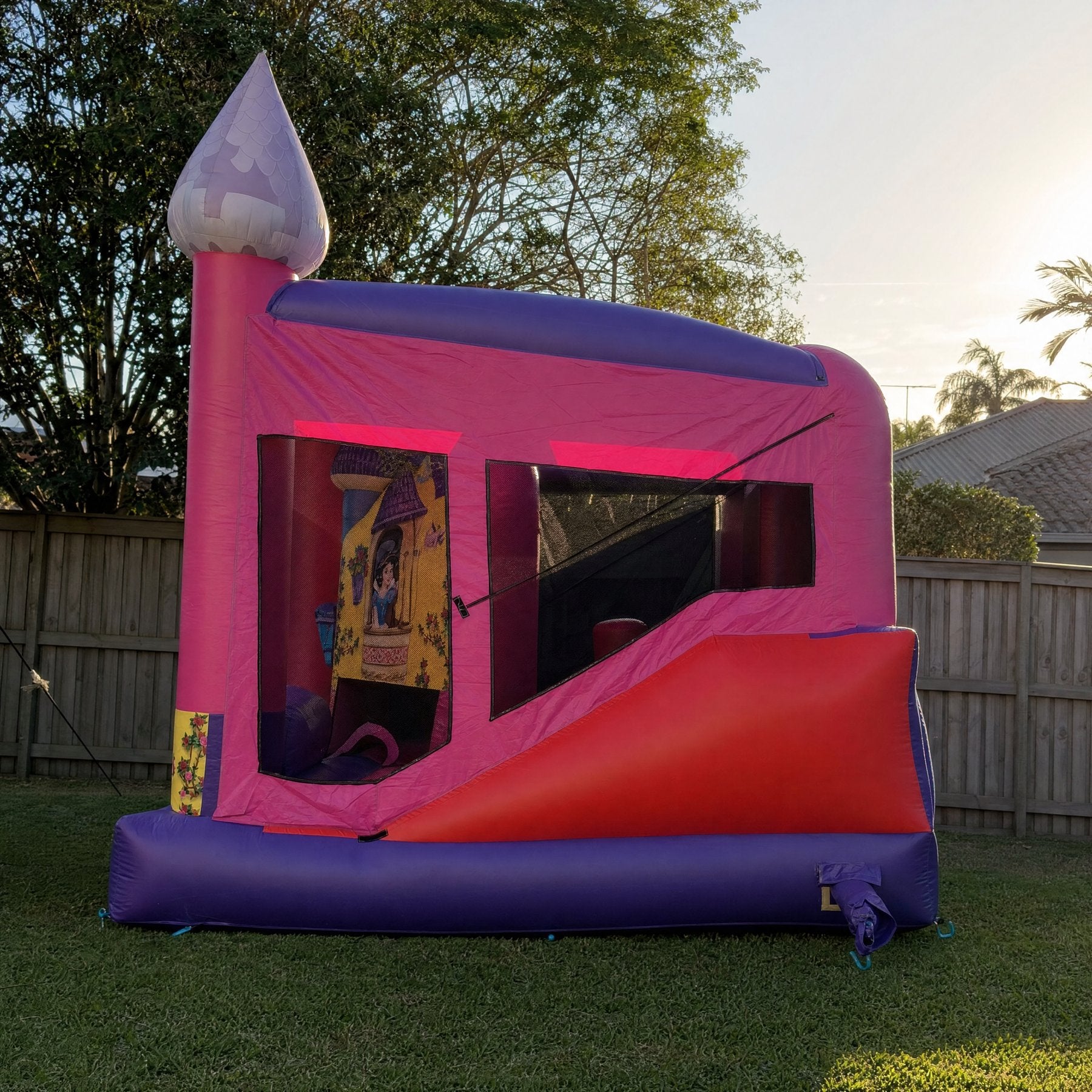 Side profile of a pink and purple jumping castle combo with a red slide