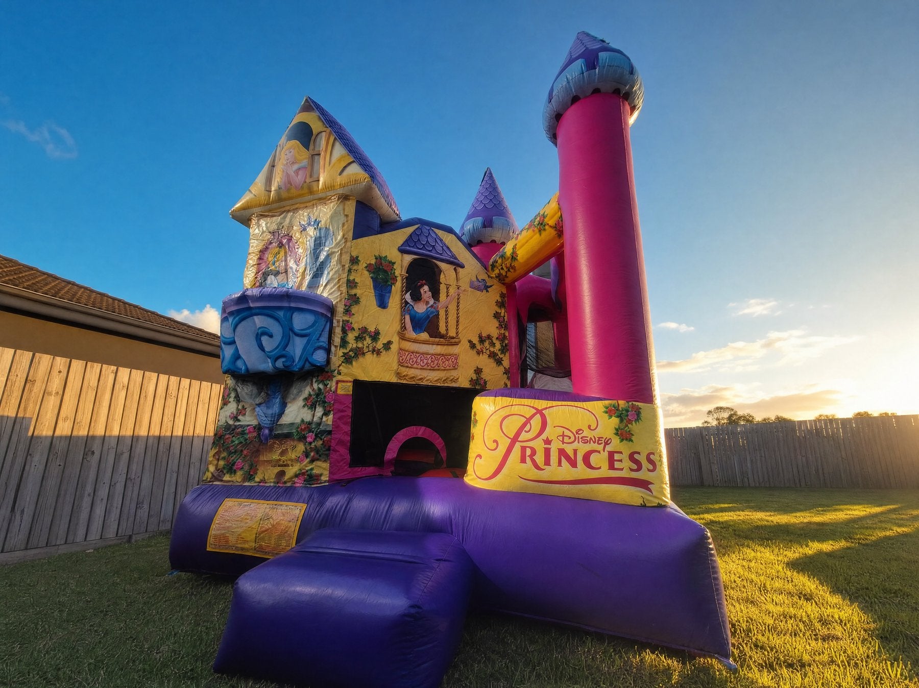 Low-angle wide view of a Disney Princess jumping castle combo at golden hour
