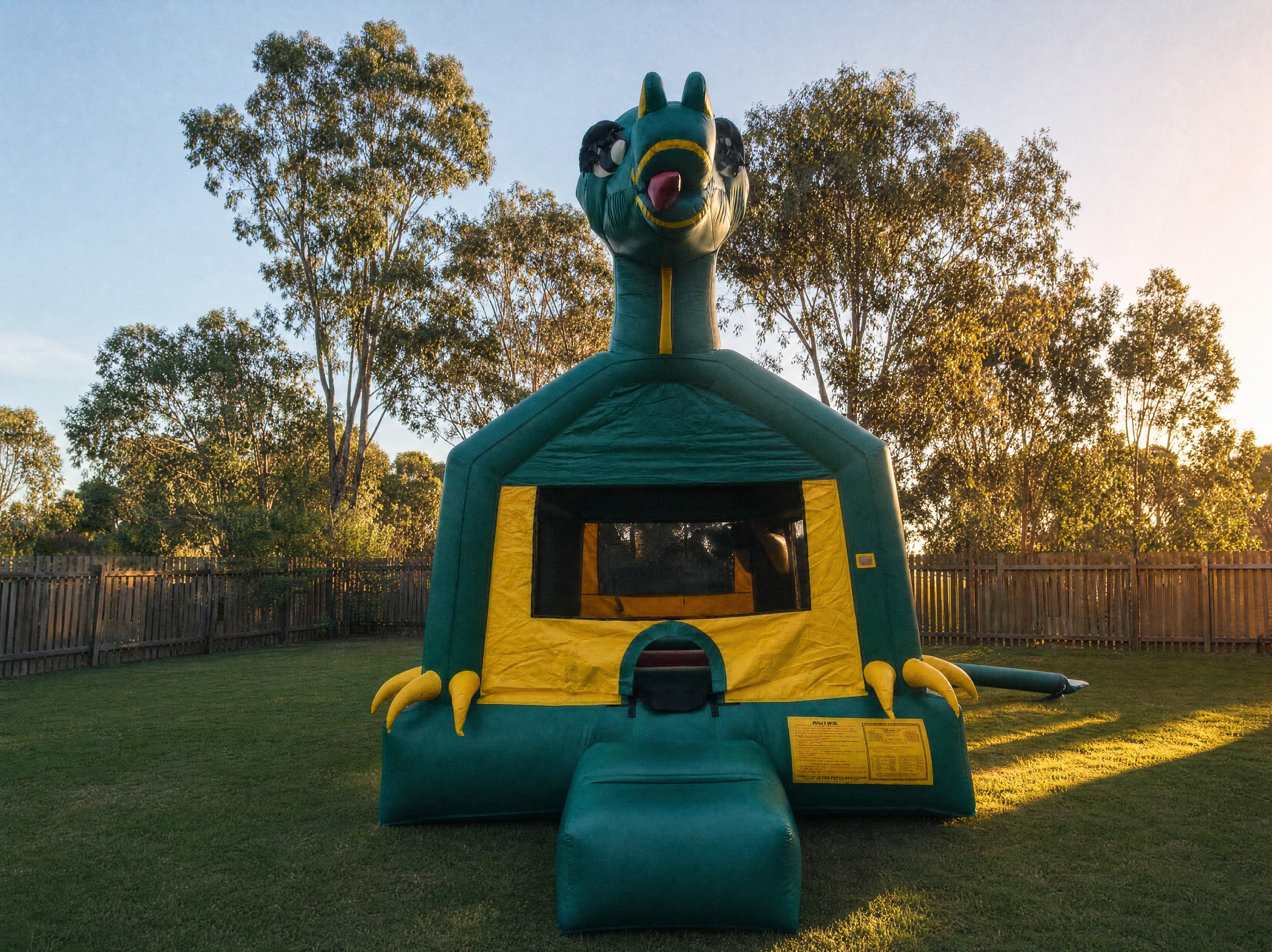 Green Dinosaur Jumping Castle hire, wide front view showing the full dinosaur head, claws, and entrance at backyard scale