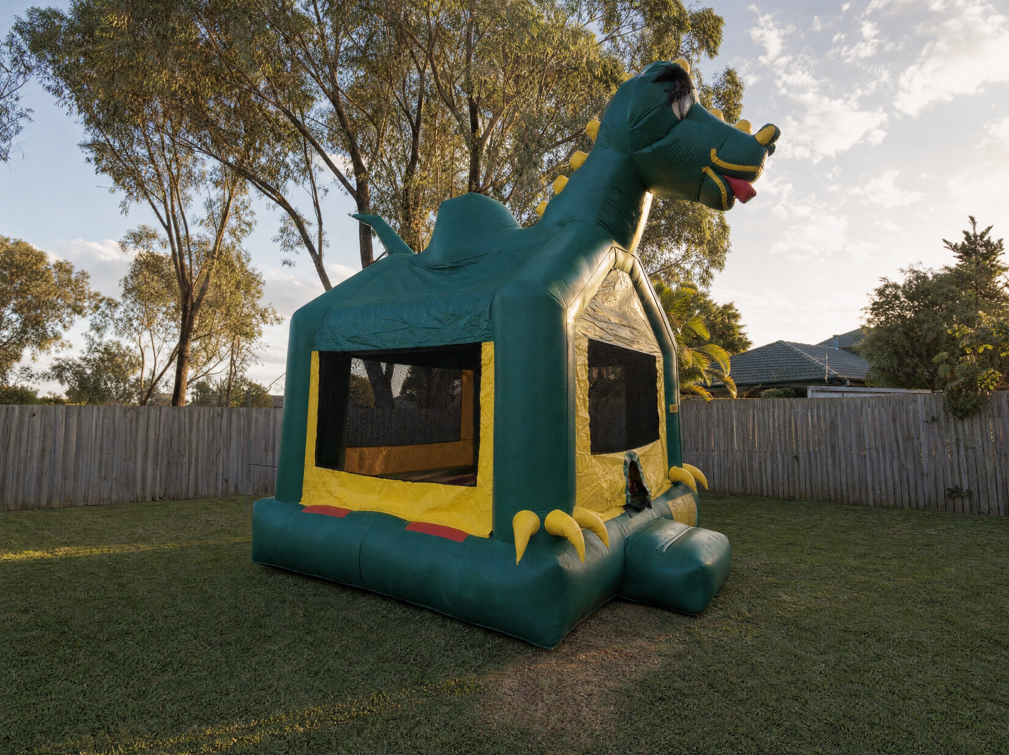 Green Dinosaur Jumping Castle hire, wide desktop view showing full backyard fit
