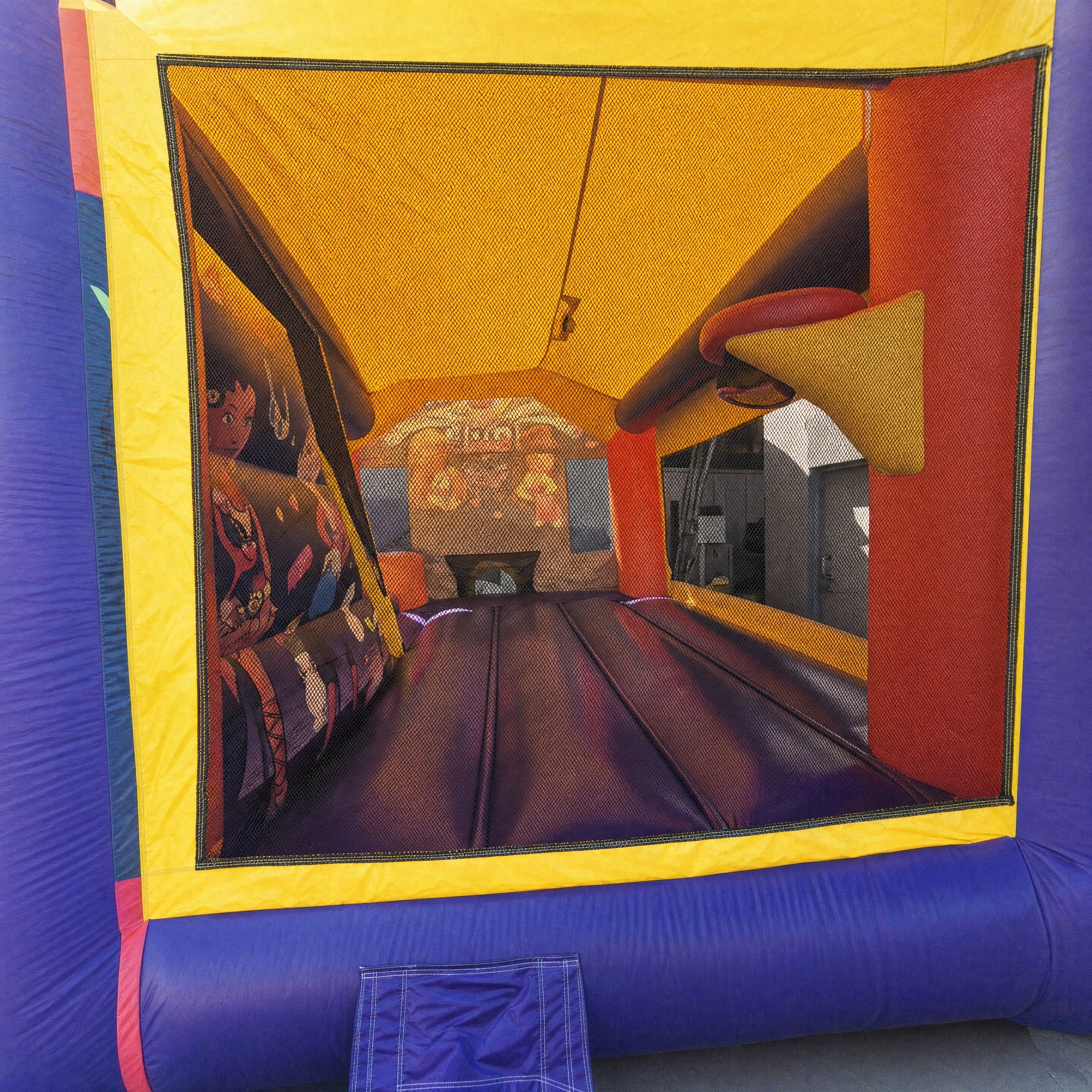 Interior view into a jumping castle combo showing the padded bounce floor and basketball hoop