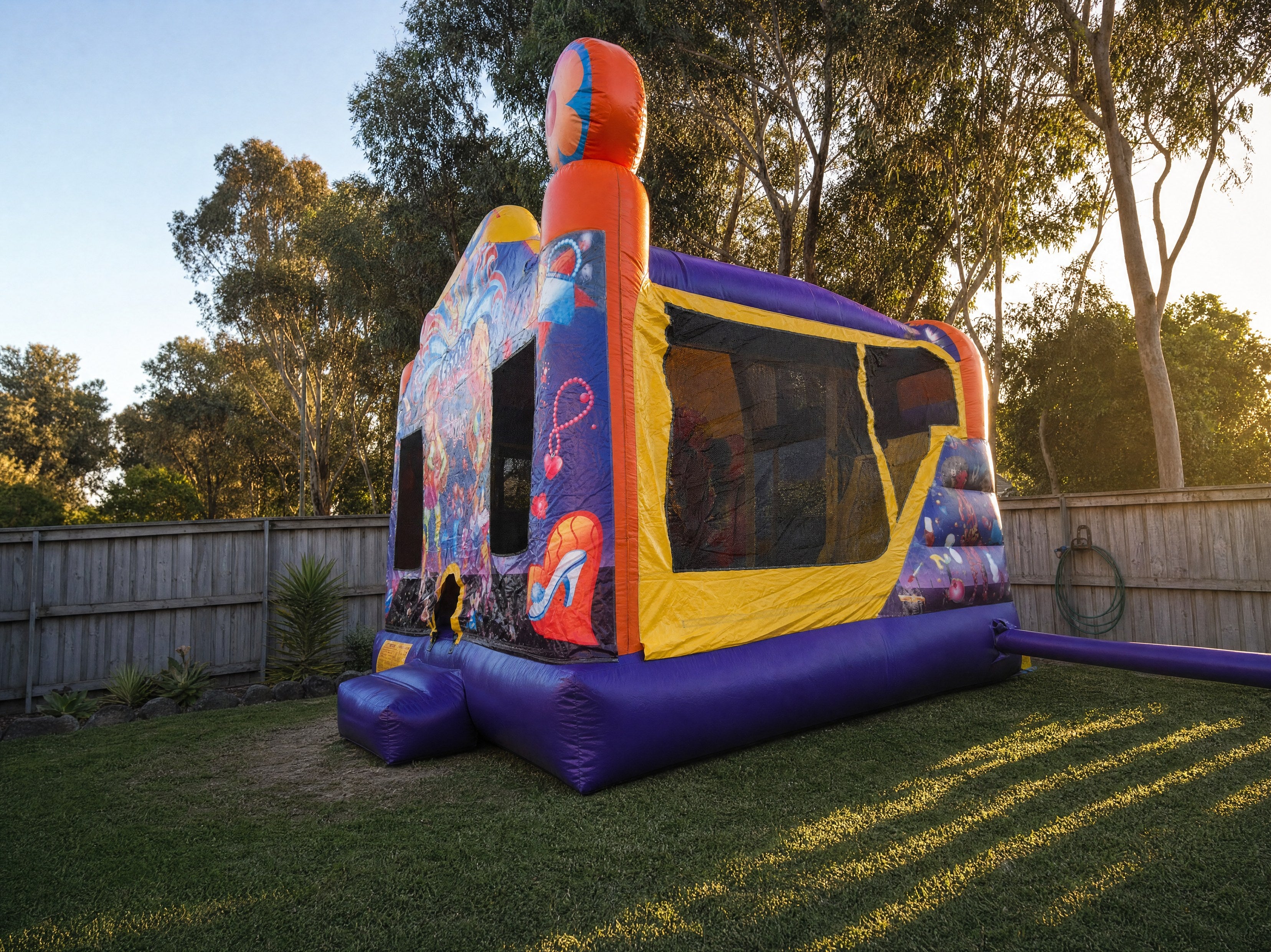 Wide backyard view of a jumping castle combo showing its true scale against a timber fence