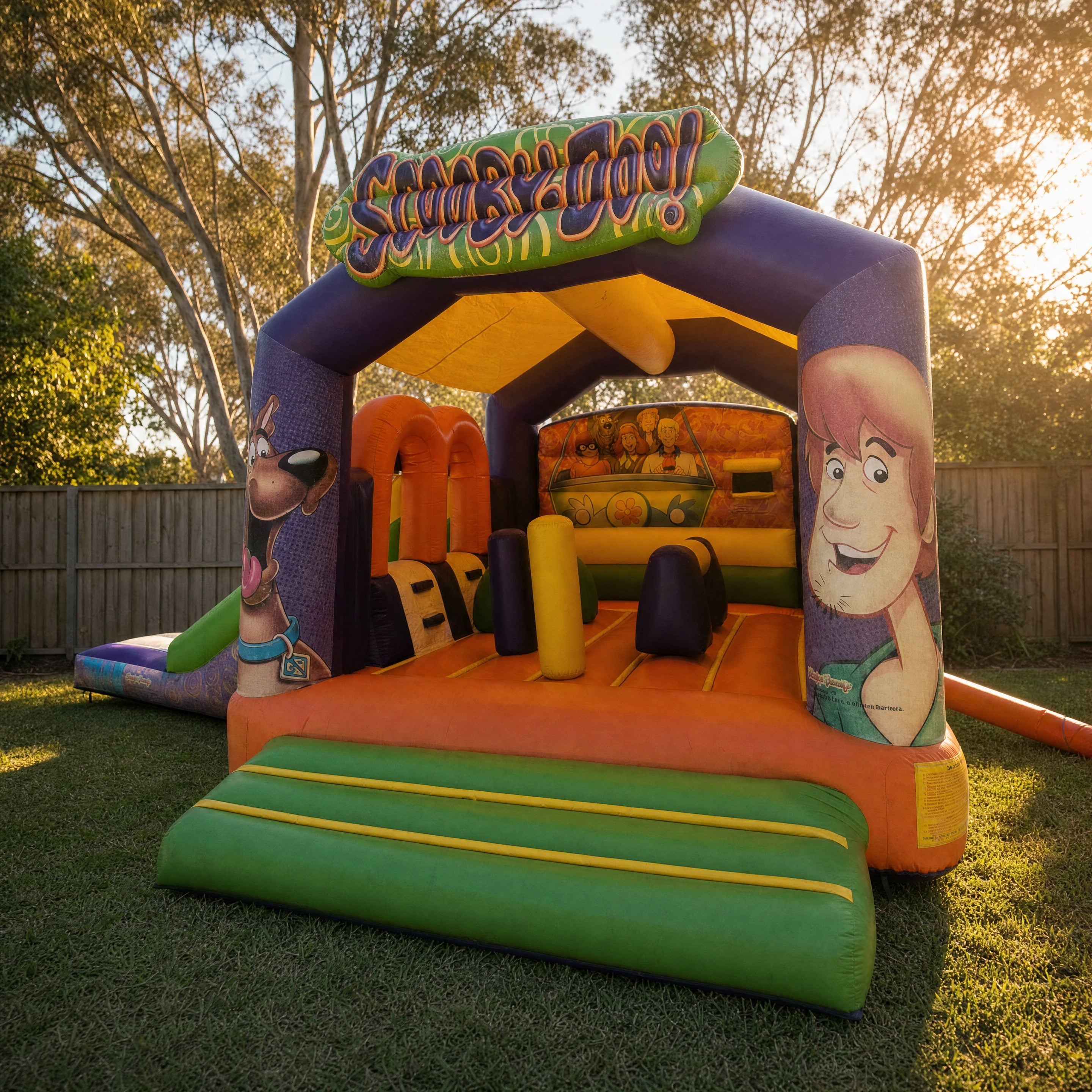 Scooby Doo with Side Slide Combo jumping castle in a backyard at golden hour showing the arch signage and character artwork