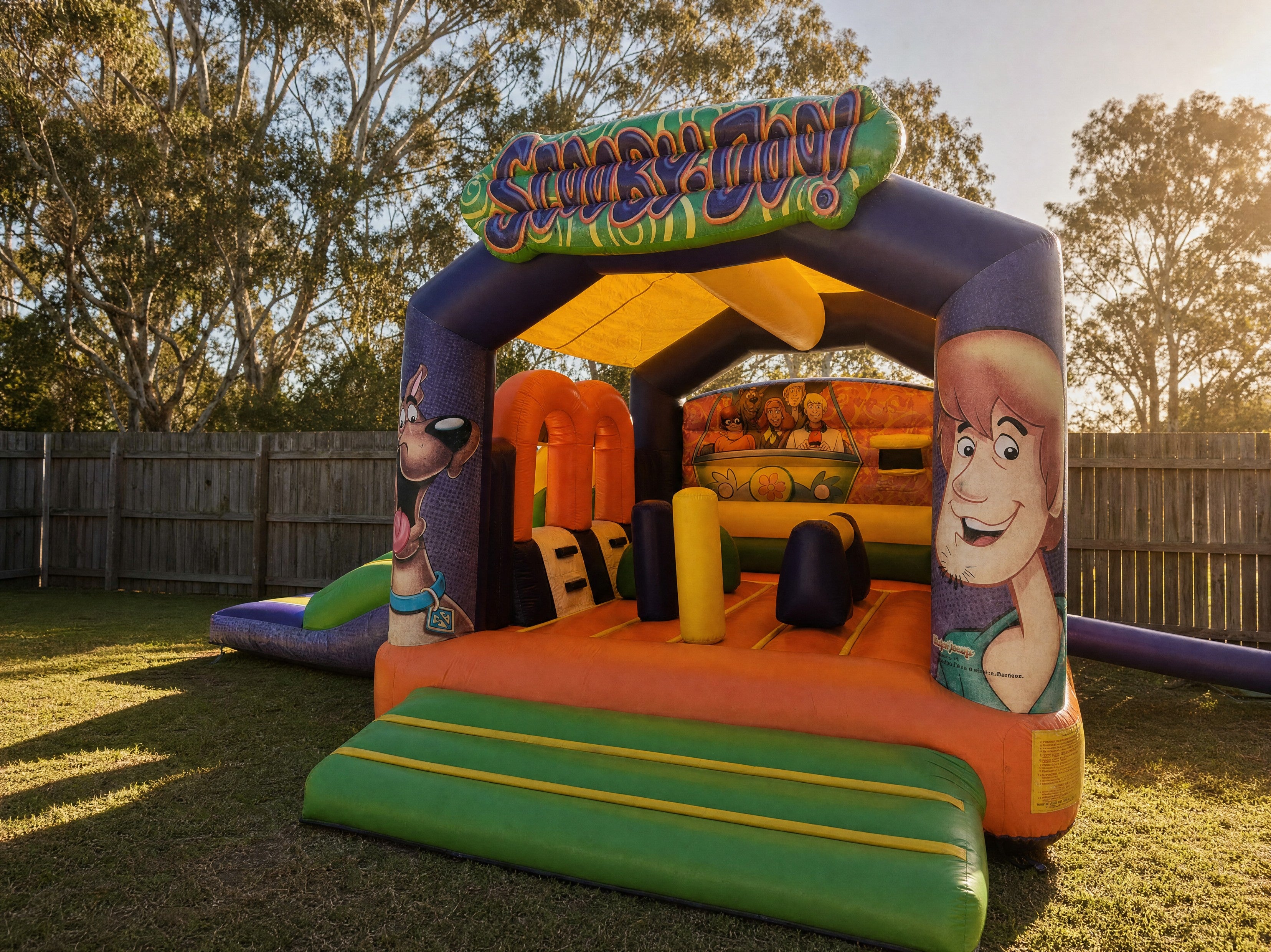Wide view of the Scooby Doo with Side Slide Combo jumping castle in a backyard at golden hour