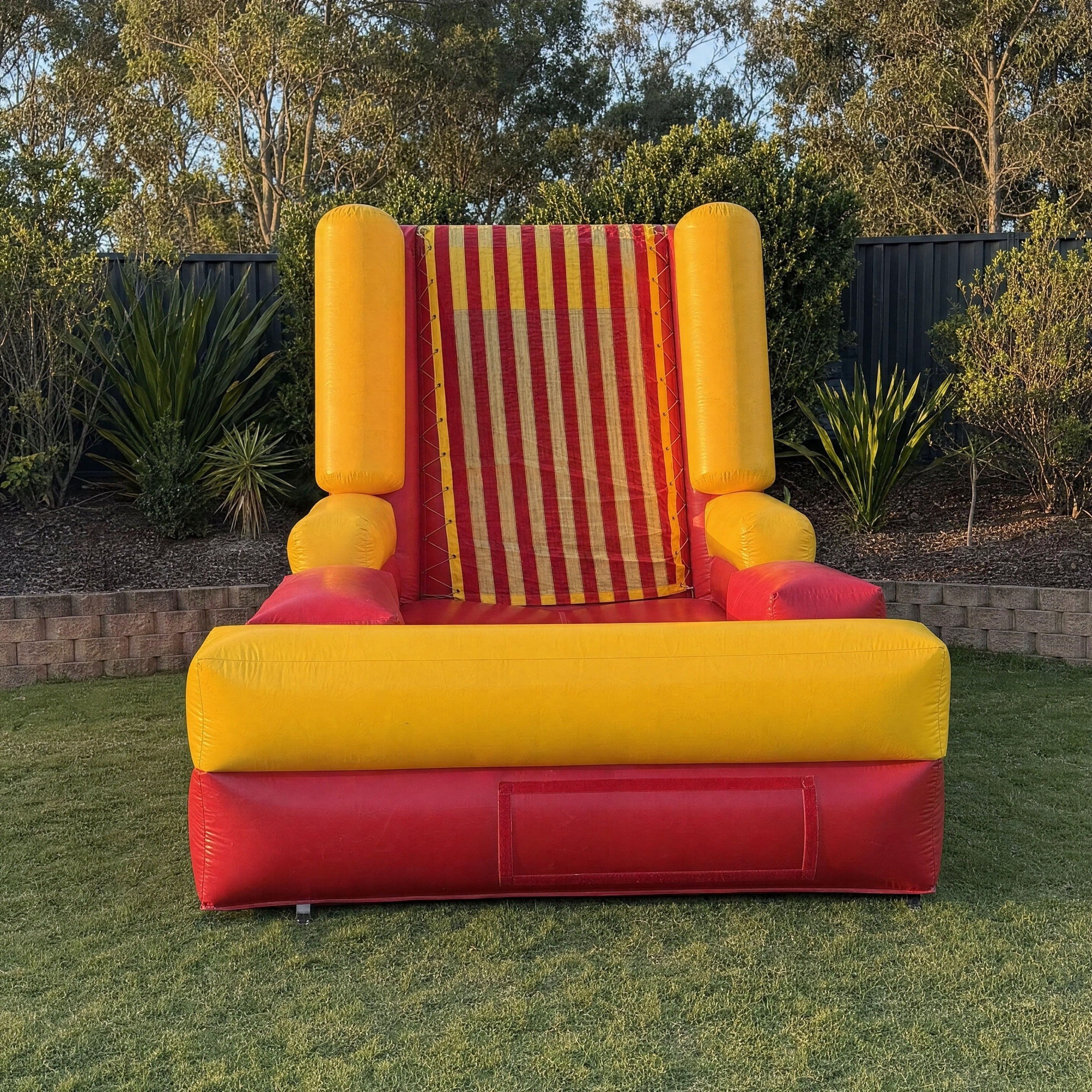Sticky Wall inflatable game positioned in a garden with fencing visible behind it