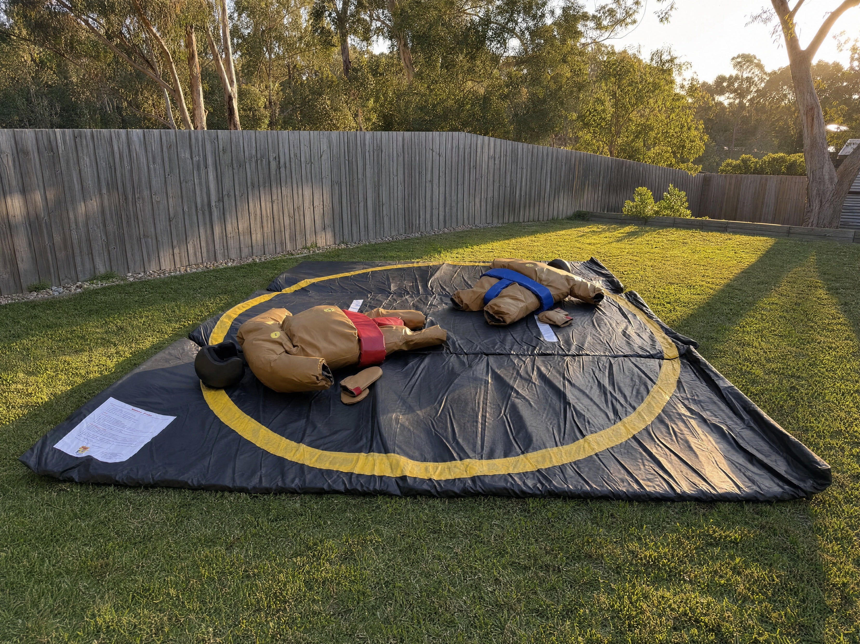 Wide pulled-back view of the sumo suits ring mat in a backyard showing fence and trees