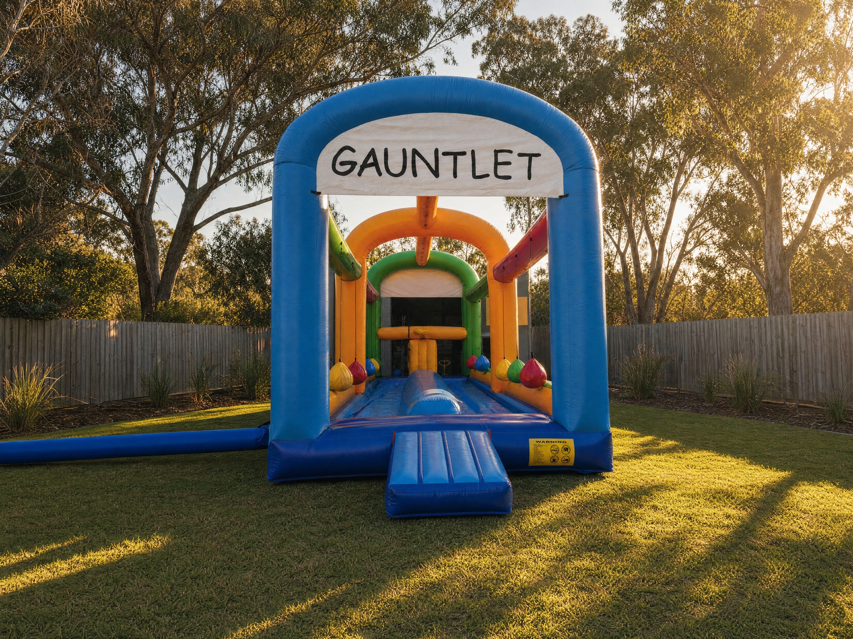Wide view of The Gauntlet inflatable obstacle course showing its full length in a backyard
