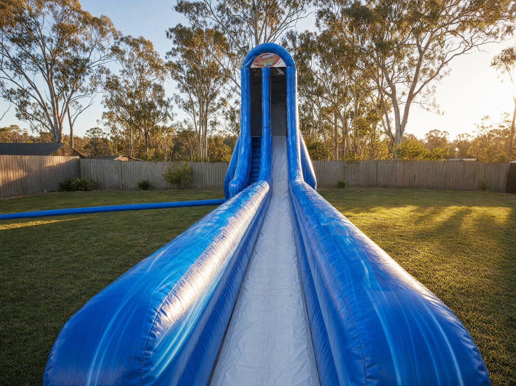 Vertical Screamer Water Slide Hire towering over a Central Coast backyard at golden hour, full length wide view
