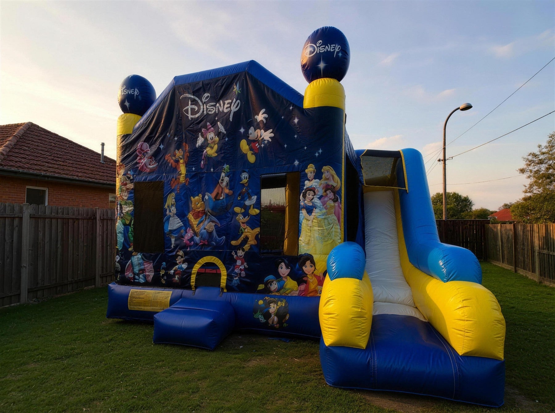 World of Disney C7 Combo jumping castle with slide set up in a Central Coast backyard at golden hour